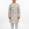Boy wearing white and brown printed Indian ethnic kurta with white churidar pants, standing barefoot