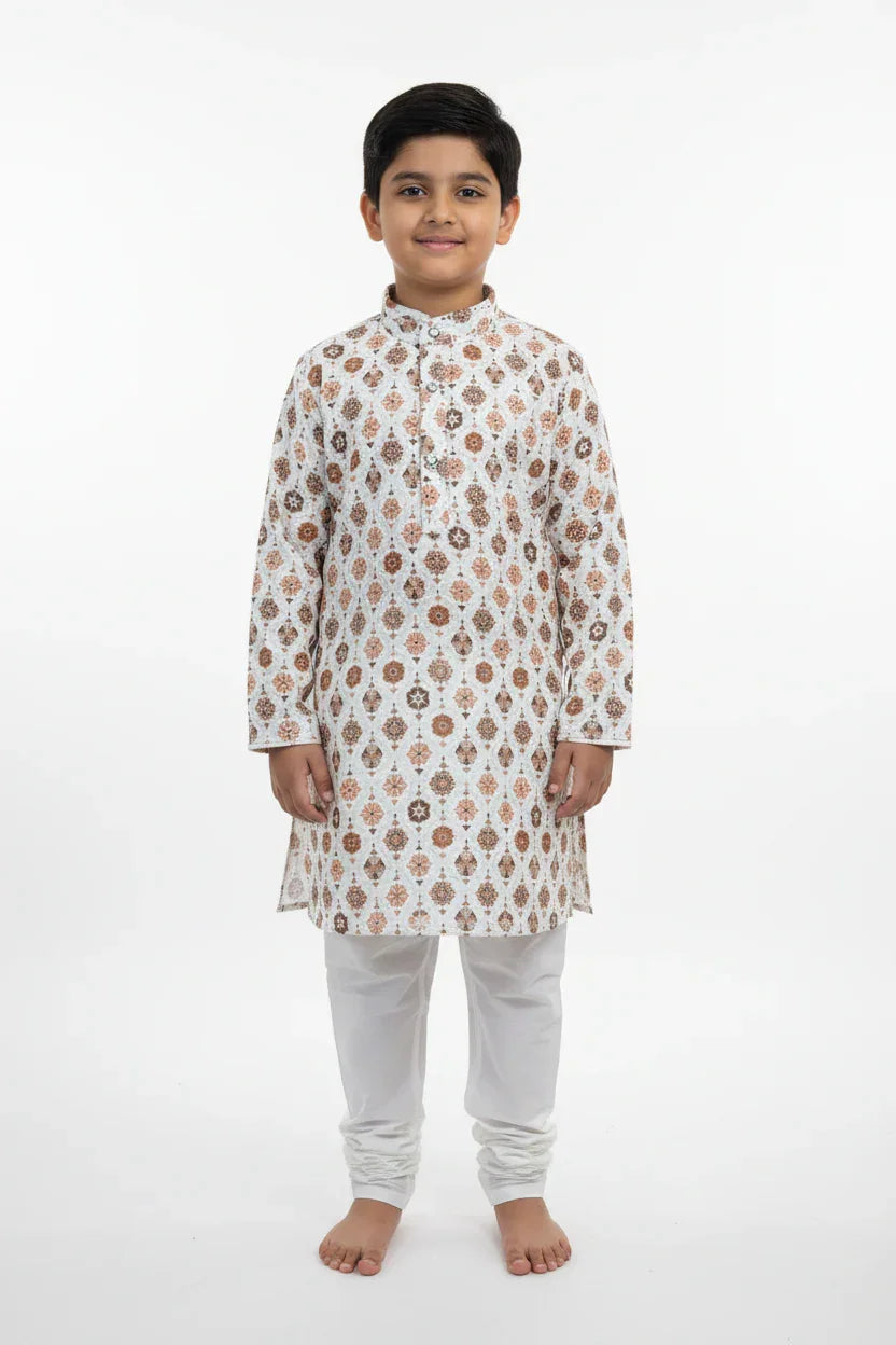 Boy wearing white and brown printed Indian ethnic kurta with white churidar pants, standing barefoot