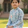 Young boy in light blue floral printed Indian ethnic kurta with white pants sitting outdoors in garden