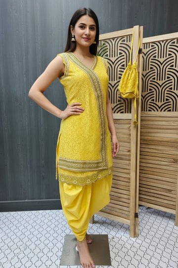 Woman in sleeveless yellow embroidered Indian ethnic kurta with matching dupatta bag and dhoti pants, standing indoors