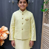 Boy in yellow Indian ethnic wear kurta and jacket standing indoors with decorative wooden panel and flower