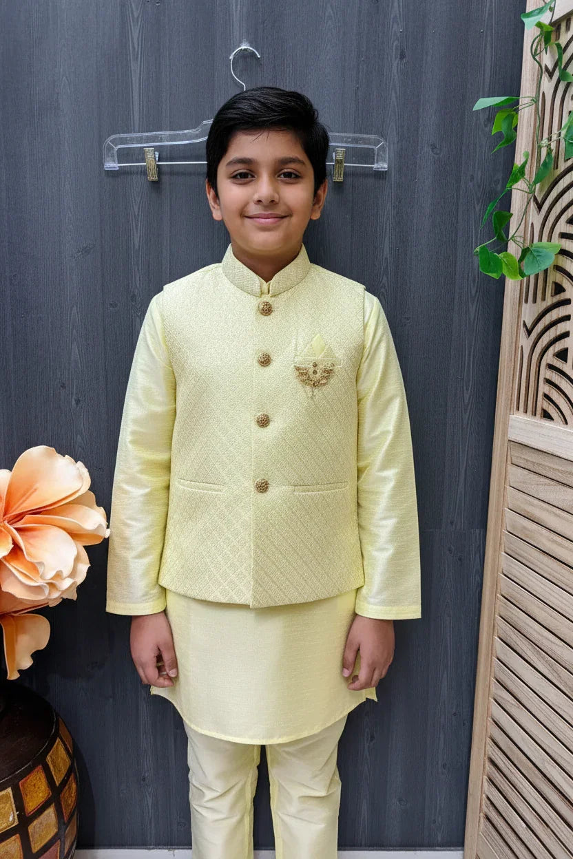 Boy in yellow Indian ethnic wear kurta and jacket standing indoors with decorative wooden panel and flower