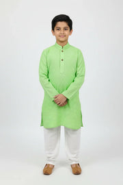 Young boy wearing light green kurta with white churidar and brown traditional shoes on white background