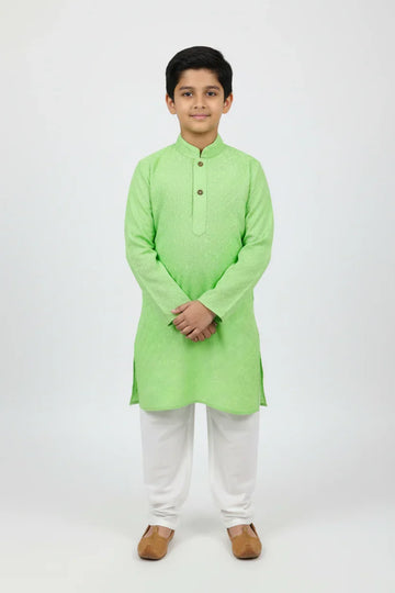 Young boy wearing light green kurta with white churidar and brown traditional shoes on white background