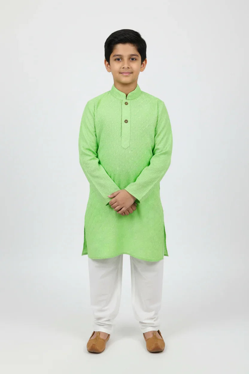 Young boy wearing light green kurta with white churidar and brown traditional shoes on white background
