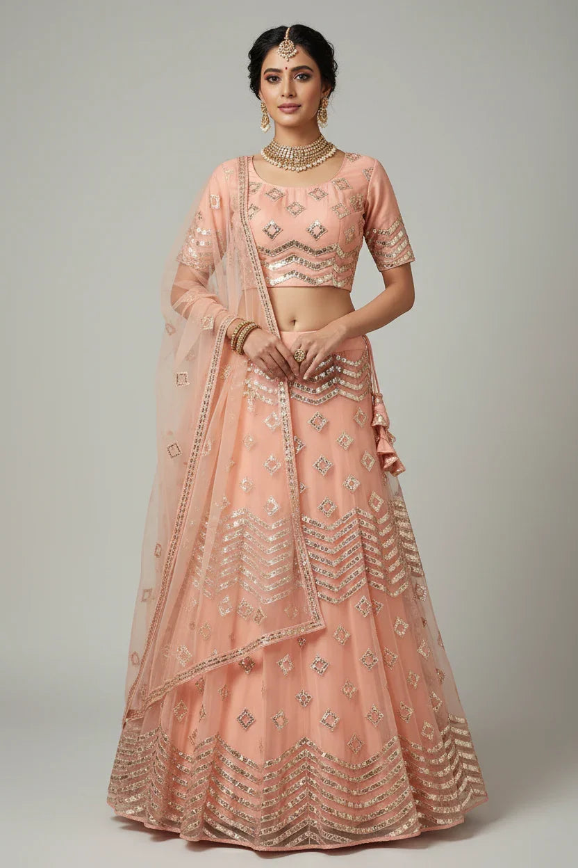 Woman in peach Indian ethnic lehenga with gold sequin embroidery and matching jewelry, posing against light background