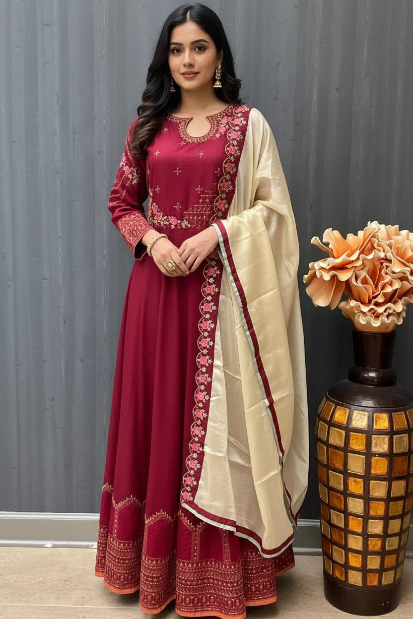 Woman in maroon embroidered Indian ethnic dress with cream dupatta standing by decorative vase