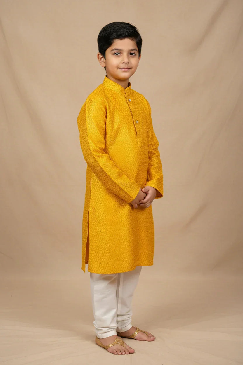 Young boy wearing a mustard yellow Indian kurta with white churidar pants and traditional sandals