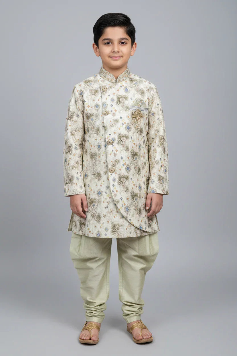 Boy wearing cream-colored traditional Indian sherwani with intricate patterns and churidar pants at Anandi Fashions